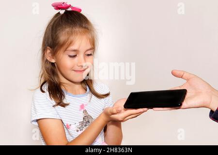 Submit a smart phone to a child. The father gives the child a smartphone. Children's addiction to electronic gadgets. Concept. Stock Photo