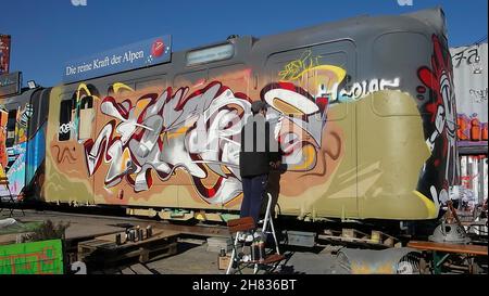 Artist spraying graffiti on a discarded train car in the Bahnwaerter Thiel culture project area, Munich, Bavaria, Germany. Stock Photo