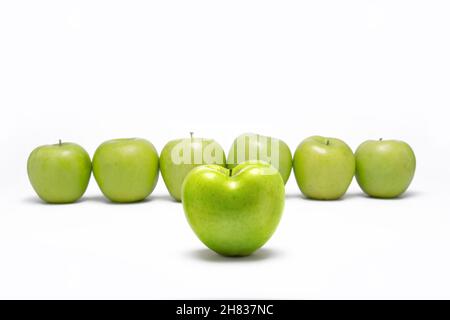 Green apple heart shaped in front of other green apples in line. On white background. Stock Photo