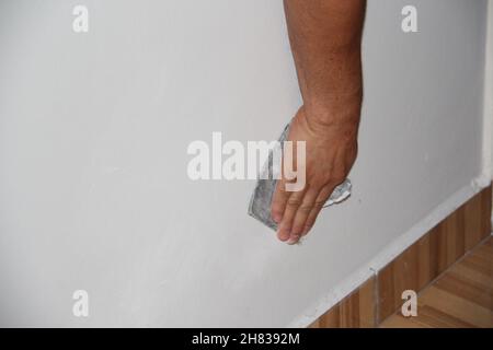 Close-up on a male hand sanding a white wall. Stock Photo