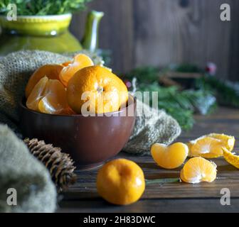 Juicy fresh tangerines lie in a brown ceramic bowl. Fir branches in the background. Stock Photo