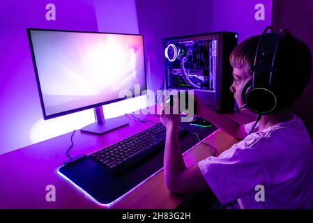 Gamer play game on gaming PC with joypad. Modern gaming setup with water cooling case, joypad, mouse, headset. Stock Photo