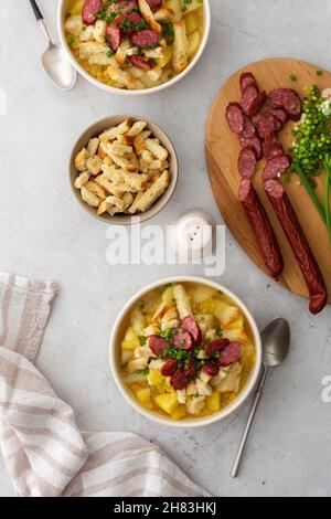 Potato and yellow pea soup with croutons and smoked meats in bowls, cutting board with chopped green onions and smoked sausage, top view Stock Photo