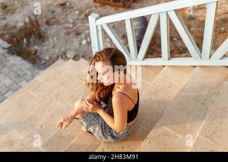 Young woman is sitting on the stairs with a sad face and looking forward.Mental health concept.Summer clothes. Stock Photo