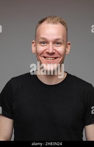 portrait of caucasian man in black t-shirt looks to the camera and smiles isolated on grey background Stock Photo