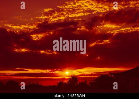 Setting sun make rays through the cloudy red sky. Stock Photo
