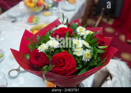 Red roses on a red satin background . fresh red roses in a bouquet as background . red roses bouquet . White chamomile rose . Stock Photo
