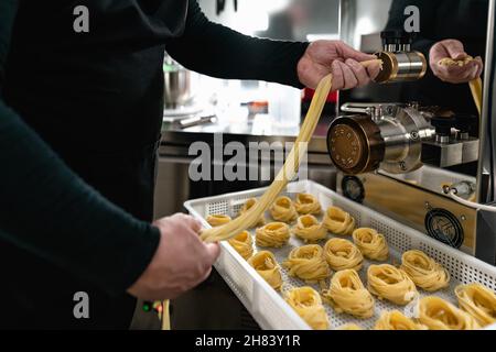 Close up male hands preparing fresh fettucine using machine inside pasta factory Stock Photo