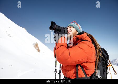 Photographer with camera taking a picture in red jacket at the snow mountains against blue sky in Almaty, Kazakhstan Stock Photo