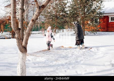 Girl cleans carpet by traditional method. Child and Caucasian woman in backyard on the background of cottage clean Persian carpet with fresh snow and Stock Photo