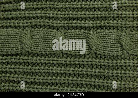 Knitted woolen green background, part of sweater or poolower, backdrop for product. Knitted wool texture, cable stitch pattern, handmade cloth Stock Photo