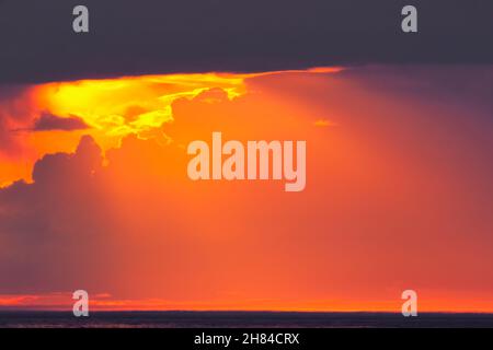 Pure bright orange sky between dark clouds overhead and blue water below Stock Photo