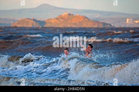 Portobello, Edinburgh, Scotland, UK. 27th November 2021. Temperature of 2 degrees and large waves from the remnants of Storm Arwen did not stop Edinburgh University students Elly and Fraser from having an exceptionally chilly afternoon dip in the Firth of Forth. Credit: Arch White Stock Photo