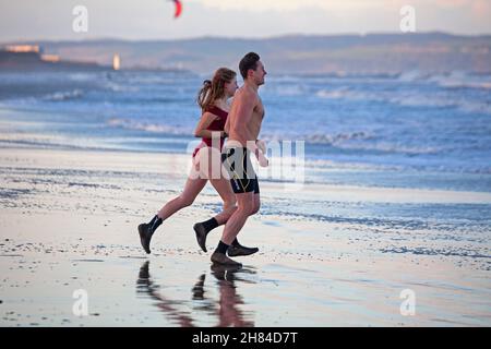 Portobello, Edinburgh, Scotland, UK. 27th November 2021. Temperature of 2 degrees and large waves from the remnants of Storm Arwen did not stop Edinburgh University students Elly and Fraser from having an exceptionally chilly afternoon dip in the Firth of Forth. Credit: Arch White Stock Photo