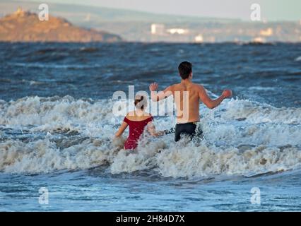 Portobello, Edinburgh, Scotland, UK. 27th November 2021. Temperature of 2 degrees and large waves from the remnants of Storm Arwen did not stop Edinburgh University students Elly and Fraser from having an exceptionally chilly afternoon dip in the Firth of Forth. Credit: Arch White Stock Photo