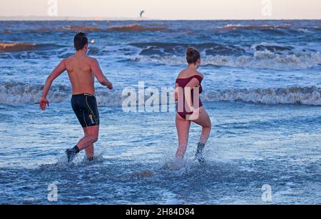 Portobello, Edinburgh, Scotland, UK. 27th November 2021. Temperature of 2 degrees and large waves from the remnants of Storm Arwen did not stop Edinburgh University students Elly and Fraser from having an exceptionally chilly afternoon dip in the Firth of Forth. Credit: Arch White Stock Photo