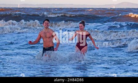 Portobello, Edinburgh, Scotland, UK. 27th November 2021. Temperature of 2 degrees and large waves from the remnants of Storm Arwen did not stop Edinburgh University students Elly and Fraser from having an exceptionally chilly afternoon dip in the Firth of Forth. Credit: Arch White Stock Photo