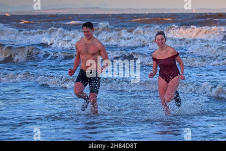 Portobello, Edinburgh, Scotland, UK. 27th November 2021. Temperature of 2 degrees and large waves from the remnants of Storm Arwen did not stop Edinburgh University students Elly and Fraser from having an exceptionally chilly afternoon dip in the Firth of Forth. Credit: Arch White Stock Photo