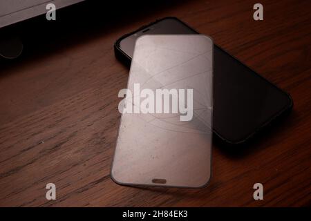 Broken smart phone screen protector film on wooden table  Stock Photo