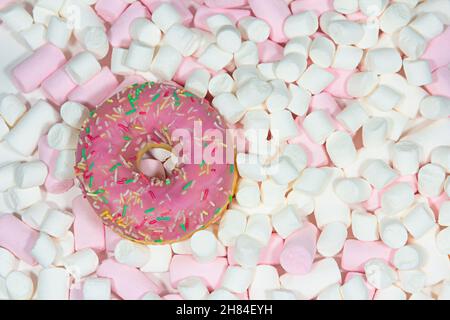 Glazed pink doughnut with colorful sugar sprikles on the pink white marshmallows background