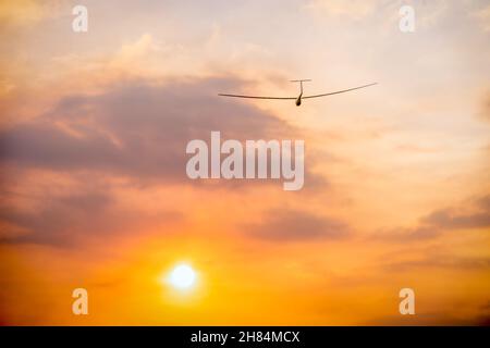 a small glider soaring over the clouds into the setting sun Stock Photo
