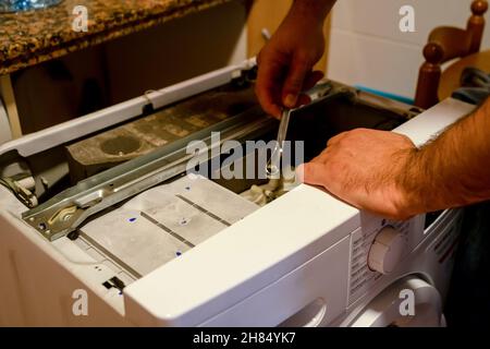 Man's hands repairing a broken washing machine that has a family unable to wash everyone's clothes Stock Photo