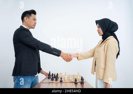Man and woman in hijab shaking hands before playing chess Stock Photo