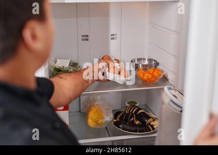 Back view portrait of unrecognizable woman taking fresh eggs out of refrigerator in kitchen, copy space Stock Photo