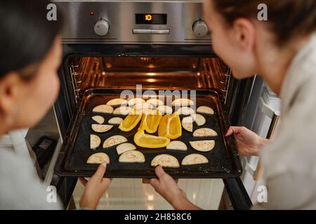High angle close up of two young women opening oven in professional kitchen, copy space Stock Photo