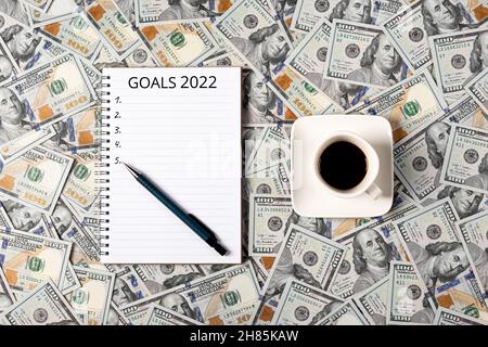 2022 goals concept banner with copy space. Notepad, pen and a cup of black coffee isolated on money background. Notepad with copy space. Office Stock Photo