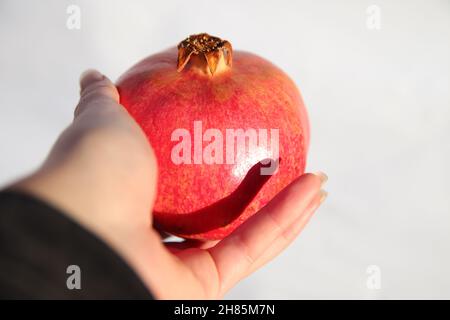 Pomegranate fruit. View from first person of female hand giving or holding ripe red pomegranate garnet fruit on white background. Isolated. Fresh and Stock Photo