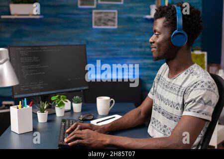 African american programmer with headphones writing program code on computer working remote from home. Employee man coding business security server. Concept of software development Stock Photo
