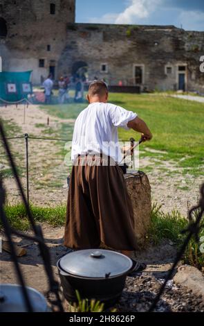 Medieval man in baggy clothes cooks food in a cauldron Stock Photo - Alamy