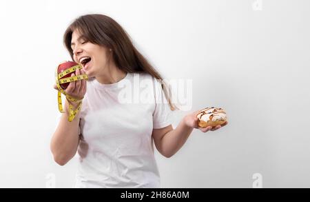 Young woman with apple and donut in hand on white background, copy space. Stock Photo