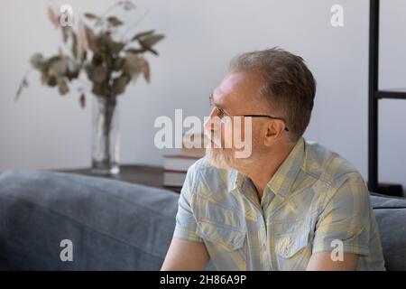 Thoughtful senior man making decision, sitting on couch at home Stock Photo