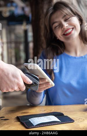 Paypass, male hands holding black pos terminal and female brings smartphone. Stock Photo