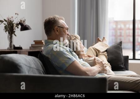 Happy senior husband embracing wife, relaxing on comfortable sofa Stock Photo