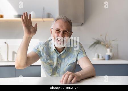 Cheerful mature 60s man in glasses waving hello at camera Stock Photo