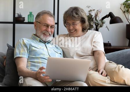 Happy mature married couple using laptop on sofa Stock Photo