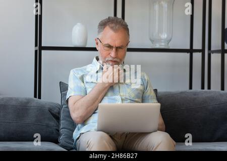 Serious senior man using online virtual app on laptop Stock Photo