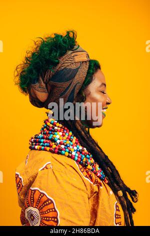 Young woman dressed in African clothing. Fashionable young woman smiling with her eyes closed while standing against a yellow background. Stylish youn Stock Photo