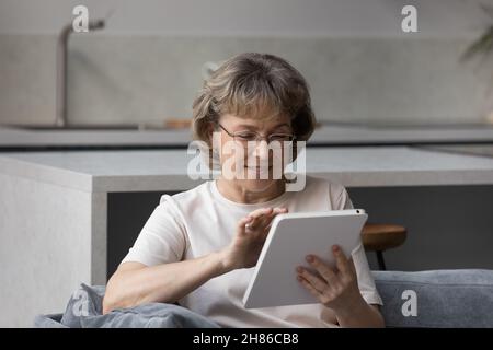 Smiling older lady using tablet computer, sitting on couch Stock Photo
