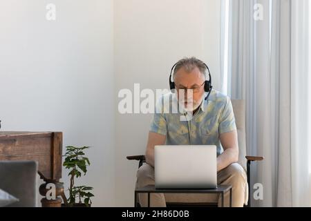 Focused older man in wireless headset using laptop at home Stock Photo