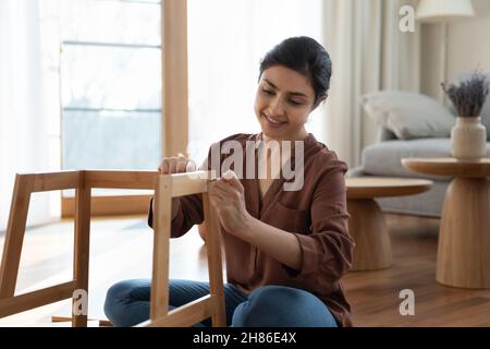 Happy beautiful young indian woman fixing chair. Stock Photo
