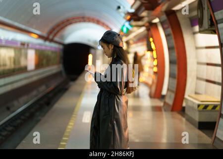 Chinese girl with smartphone at metro platform. Stylish female browsing social media wait for train Stock Photo