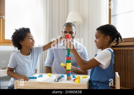 Happy Black kids playing together building high plastic tower Stock Photo