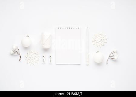 Top view photo of white christmas tree decorations notepad pen snowflakes balls snow twigs spool of thread and clothespins on isolated white backgroun Stock Photo