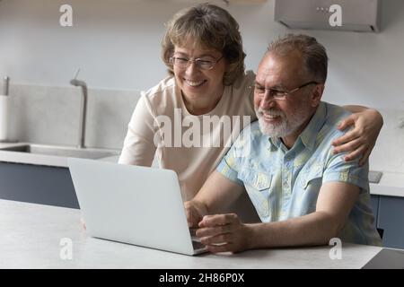 Happy old couple using laptop in kitchen, making video call Stock Photo