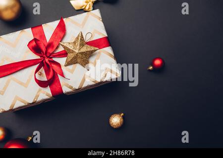 Christmas and New year present wrapped in holiday paper and decorated with red ribbon and ornaments on black background. Stock Photo