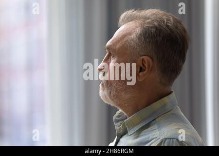 Sad thoughtful older 60s man looking out of window Stock Photo